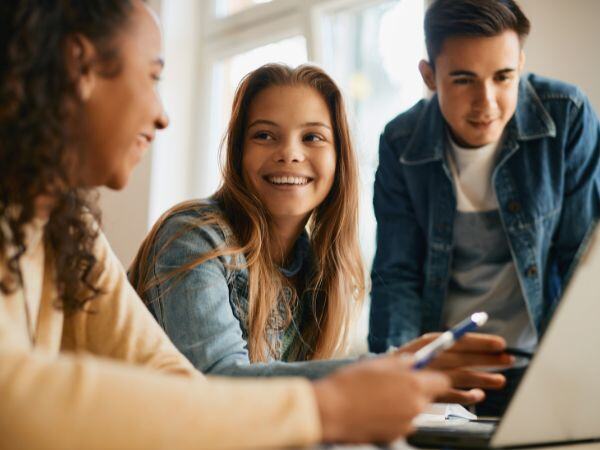 Three High School Students Looking At Laptop In Class